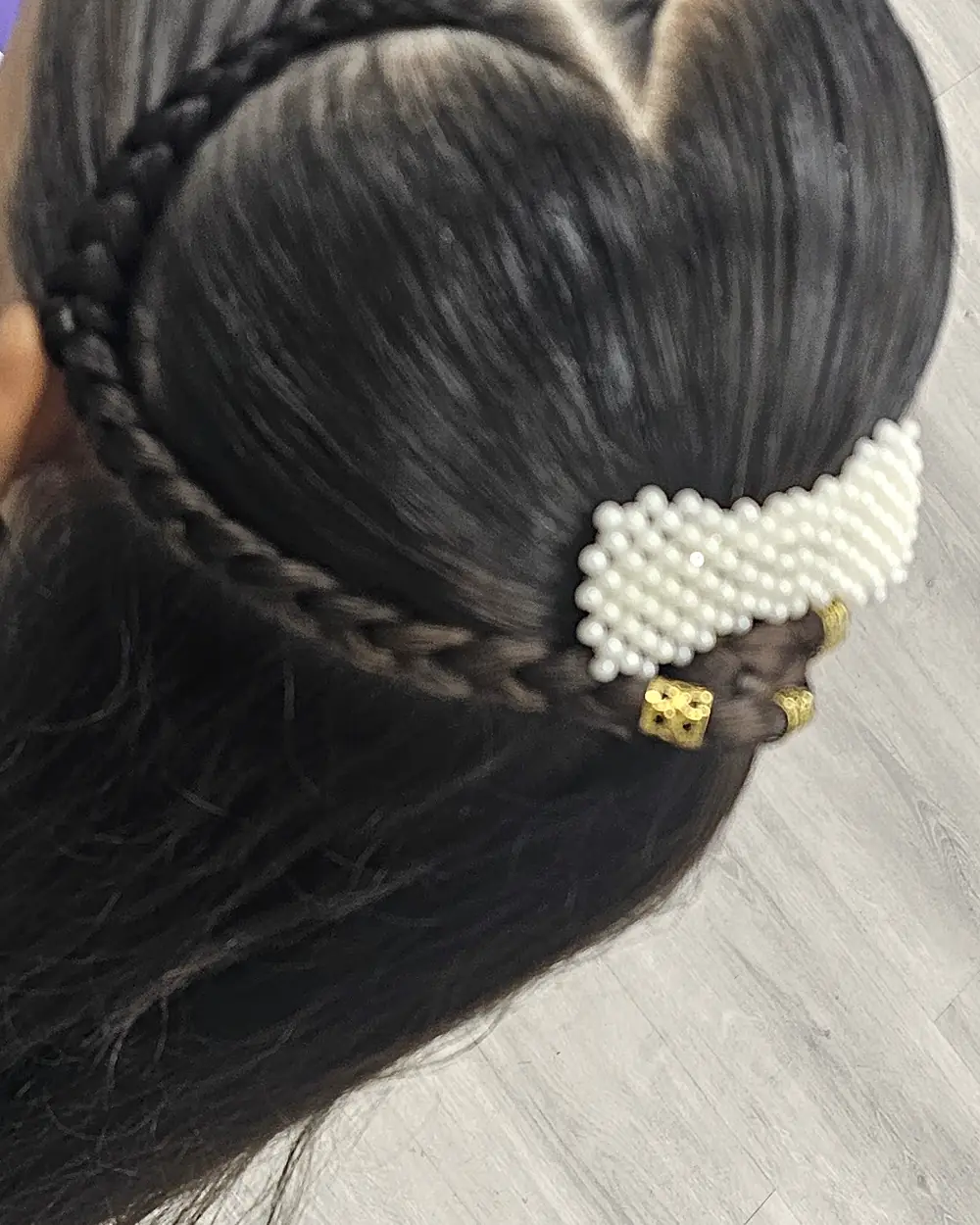 Trenza en forma de corazón vista desde arriba, rematada con una pinza de perlas.
